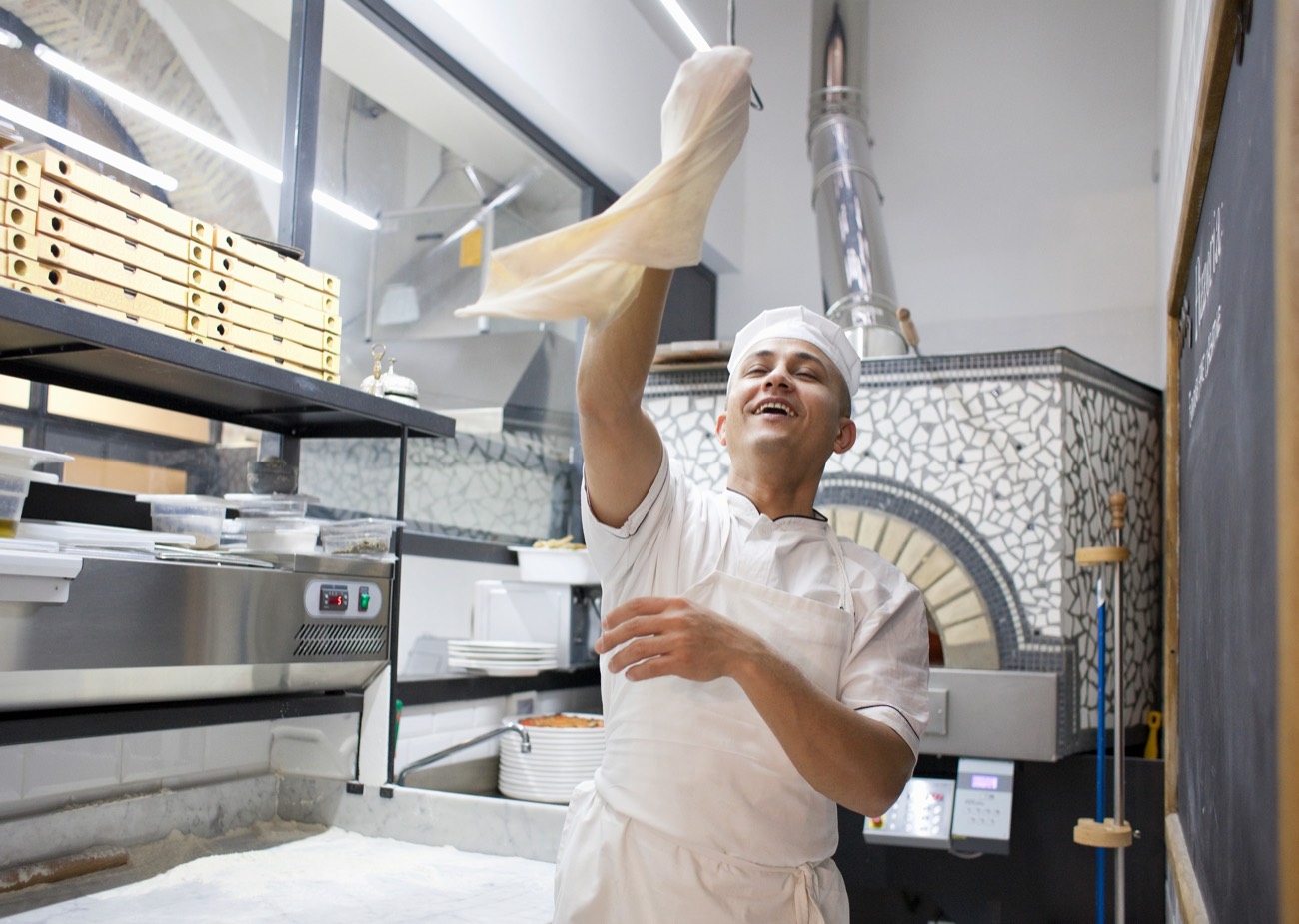Il pizzaiolo della Trattoria Pizzeria 76 lancia in aria l'impasto accanto al forno a legna